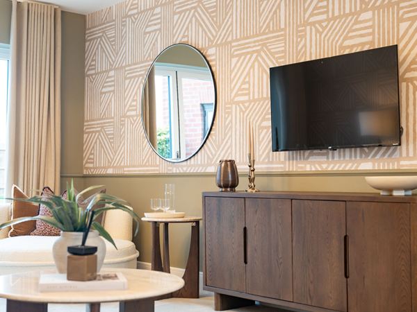 A photograph of a living room at a show home in Abbots Vale, Charles Church, with a brown TV cabinet and a round mirror on the wall.