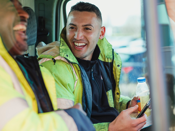 Two fireman in a van laughing together in high vis jackets