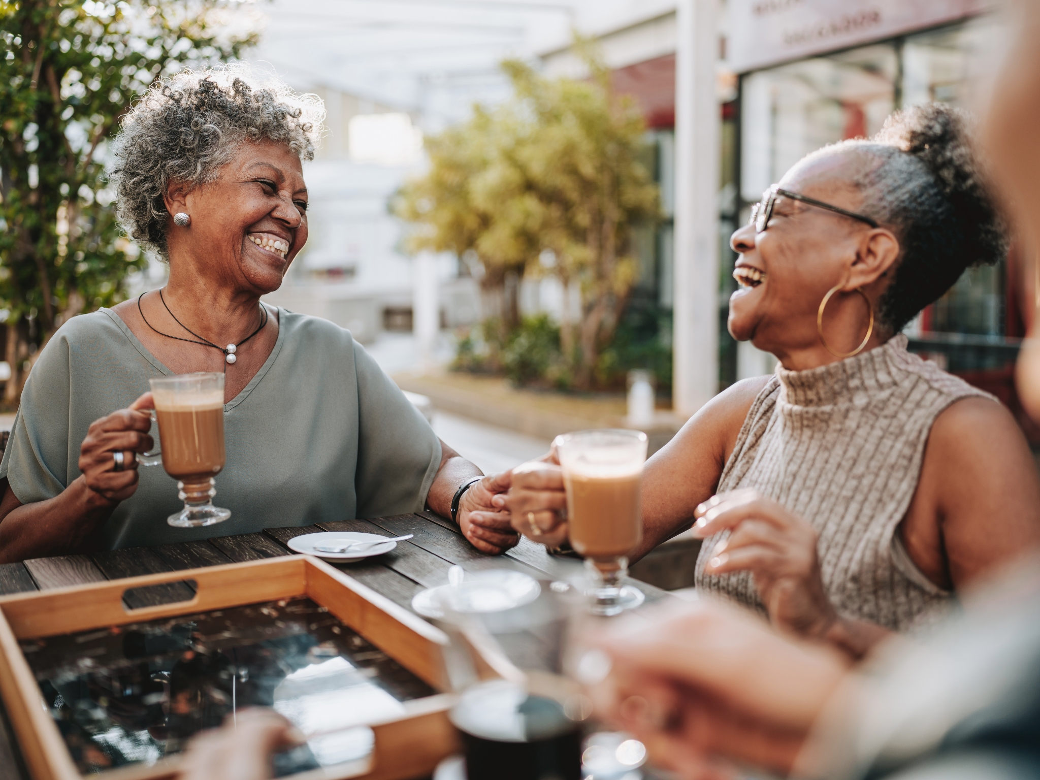 Two women laughing over coffee in a coffee shop garden.