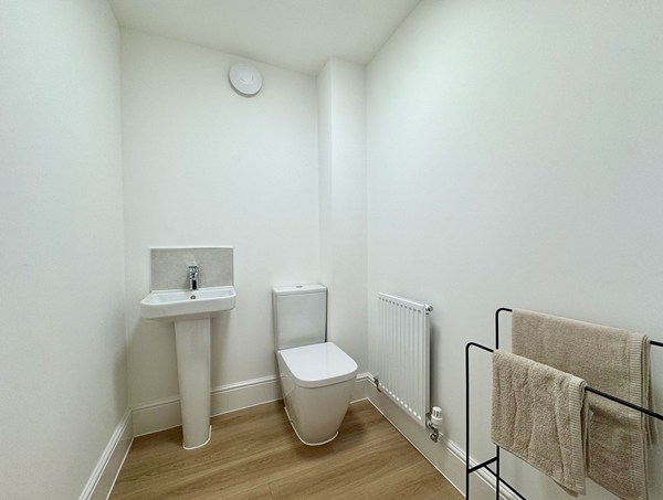 Contemporary ground floor WC in a modern new‑build home at Westwood, Curbridge, with a pedestal sink, toilet, wood‑effect flooring and simple neutral finishes.
