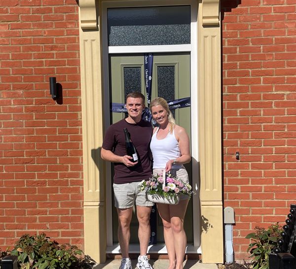 Hannah and Joe with flowers and champagne stood outside their new home