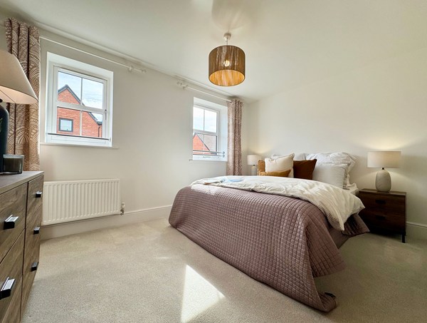 Bright third bedroom in a modern new‑build home at Westwood, Curbridge, featuring a double bed, neutral décor, soft carpet flooring and two windows bringing in natural light.