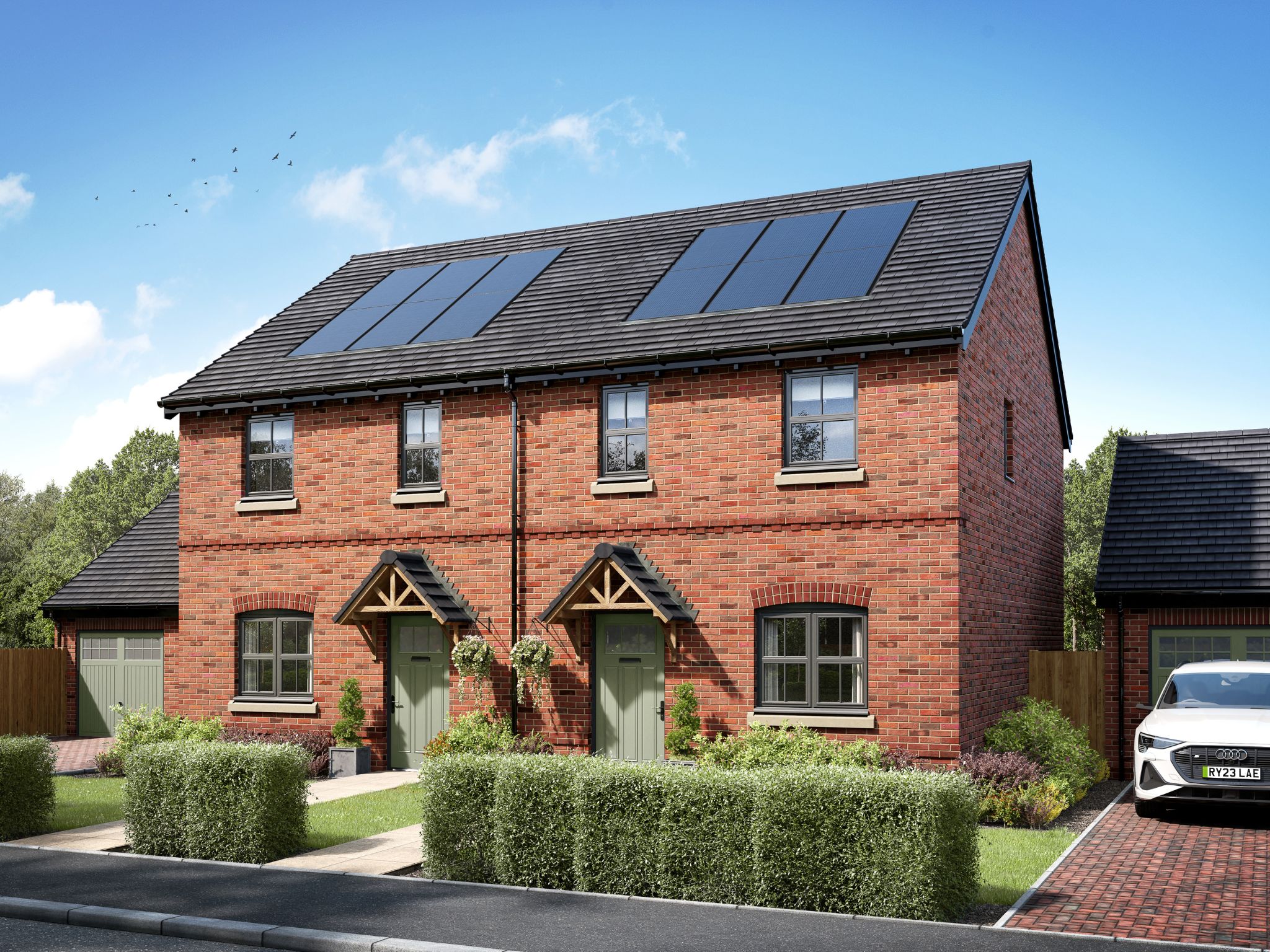 Modern red-brick semi-detached house with grey doors, pitched roof and landscaped front garden on a sunny day