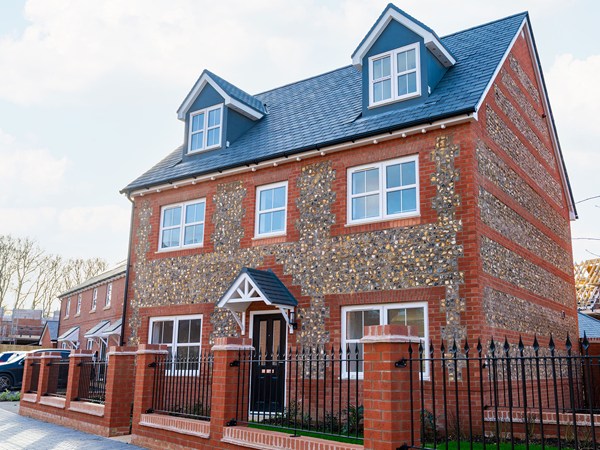 Three-storey red brick new build detached home with flint detailing, dormer windows and front garden railings.