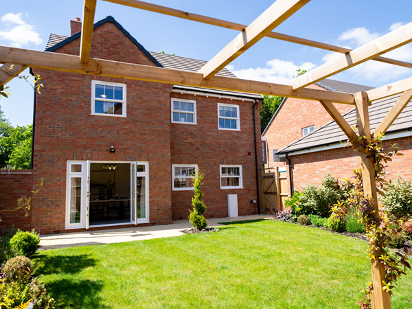 A large, premium new build home with French doors leading out into the garden with green grass and lush plants.
