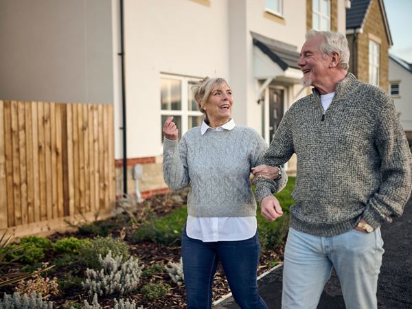 A woman and a man walking arm in arm, laughing and smiling on a modern Charles Church estate.