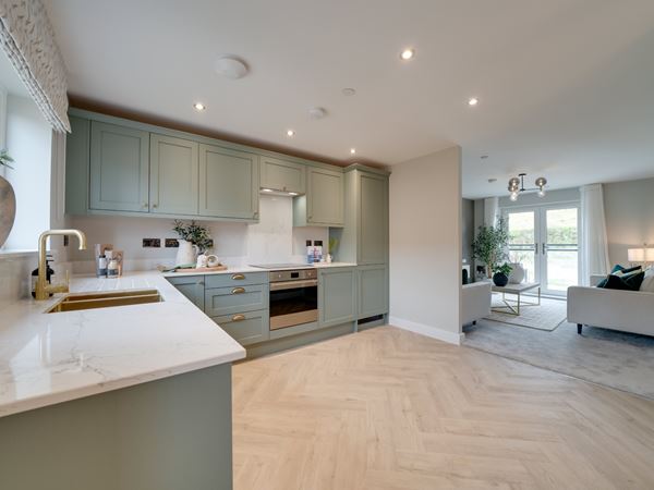 A bright and modern kitchen in a new build Charles Church home with green cabinets and a herringbone floor. 