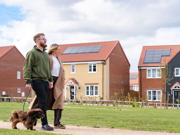 A man and a woman walking hand in hand with a dog on a new build estate by Charles Church.