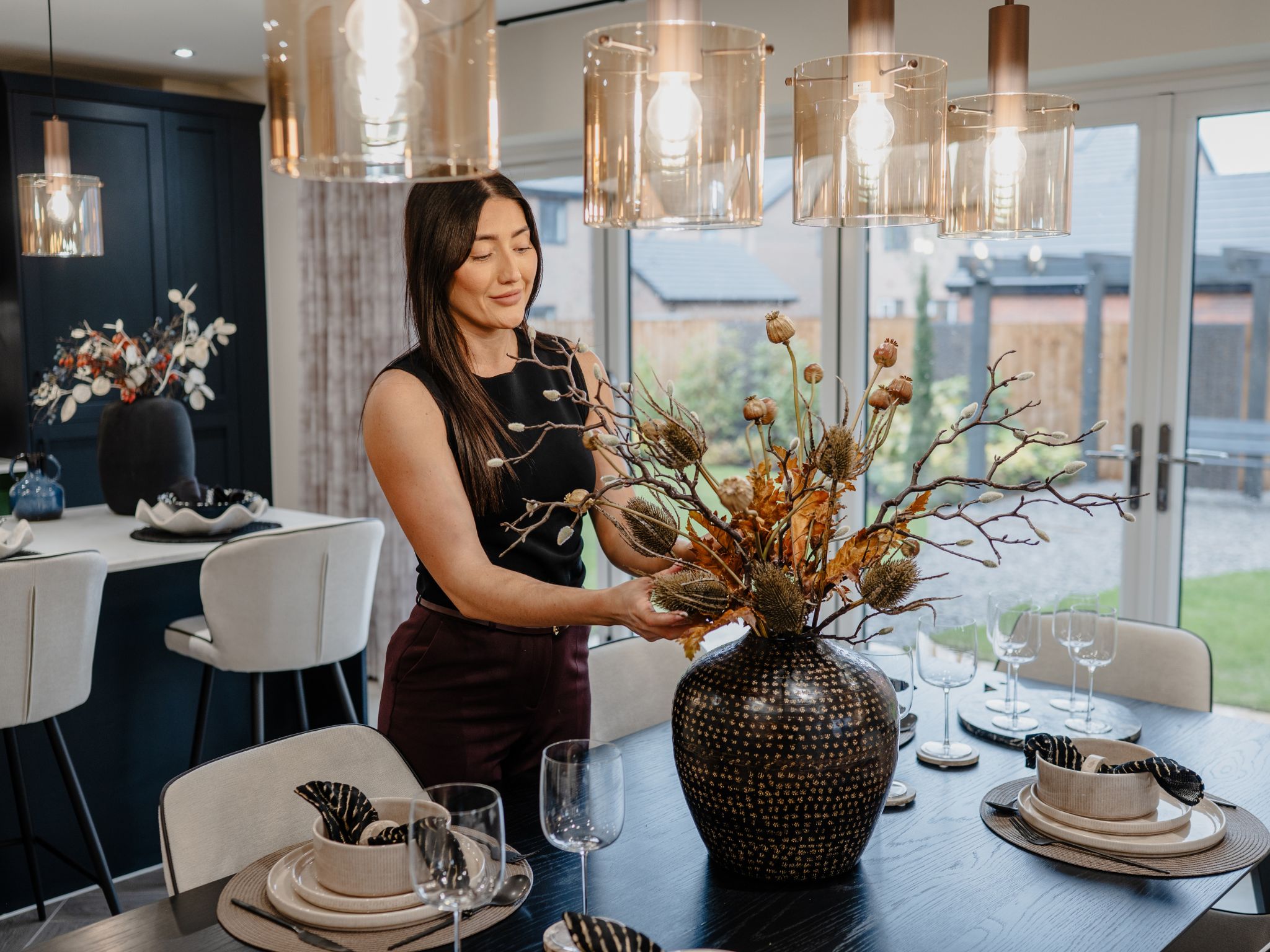 An interior designer arranging a vase of dry autumnal flowers in a new build home by Charles Church