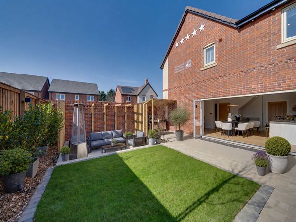A beautiful garden in a Charles Church home with a patch of grass and a seating area with a patio and bifold doors leading to the kitchen