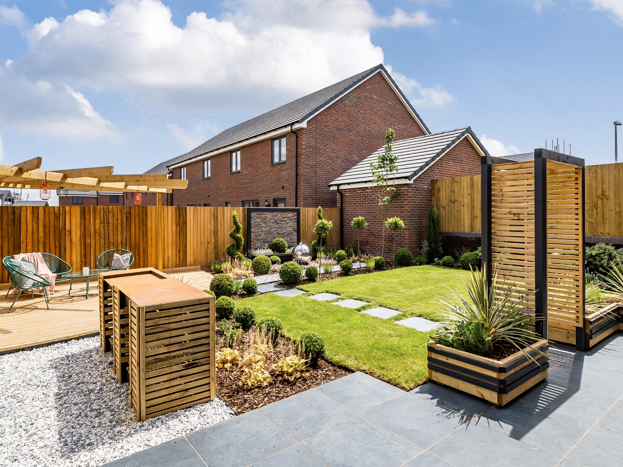 A landscaped garden in a Charles Church home, with a patio, a green section of grass, a seating area, and beautiful evergreen planting.