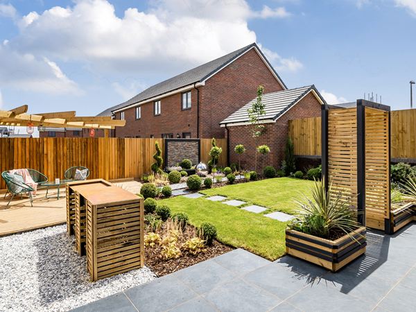 A landscaped garden in a Charles Church home, with a patio, a green section of grass, a seating area, and beautiful evergreen planting.