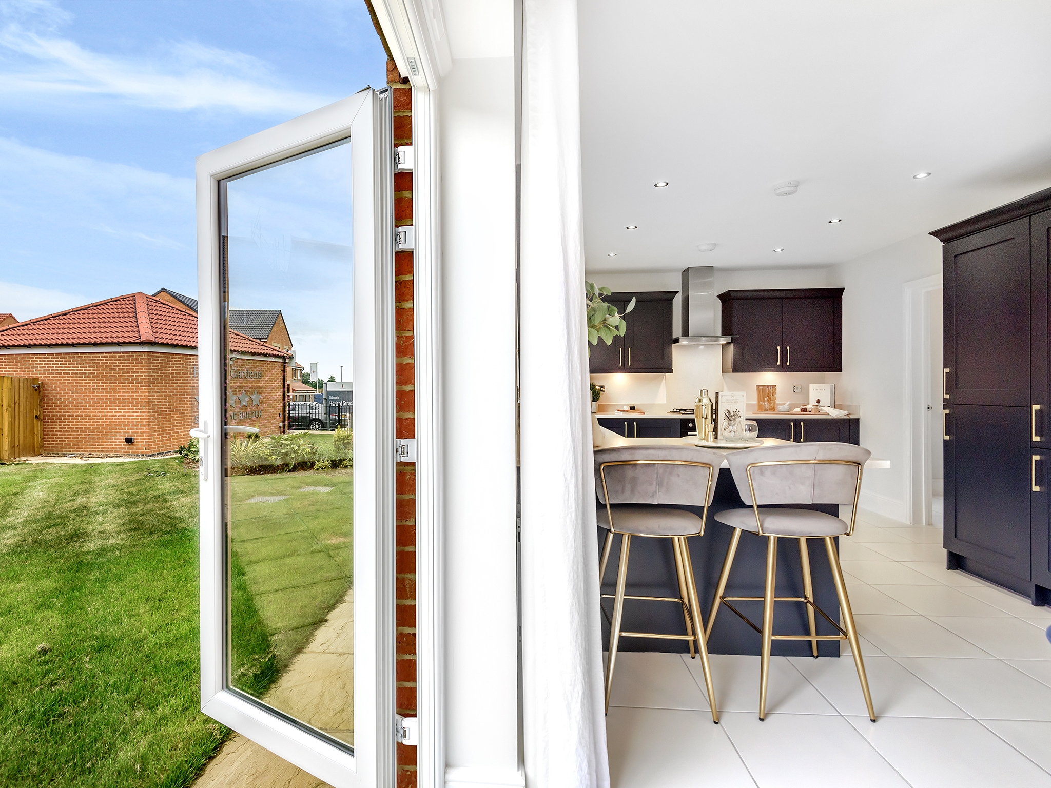 A shot of a bright and modern Charles Church kitchen with an open back door leading out onto a green lawn on a sunny day.
