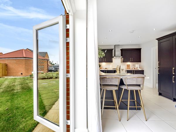 A shot of a bright and modern Charles Church kitchen with an open back door leading out onto a green lawn on a sunny day.