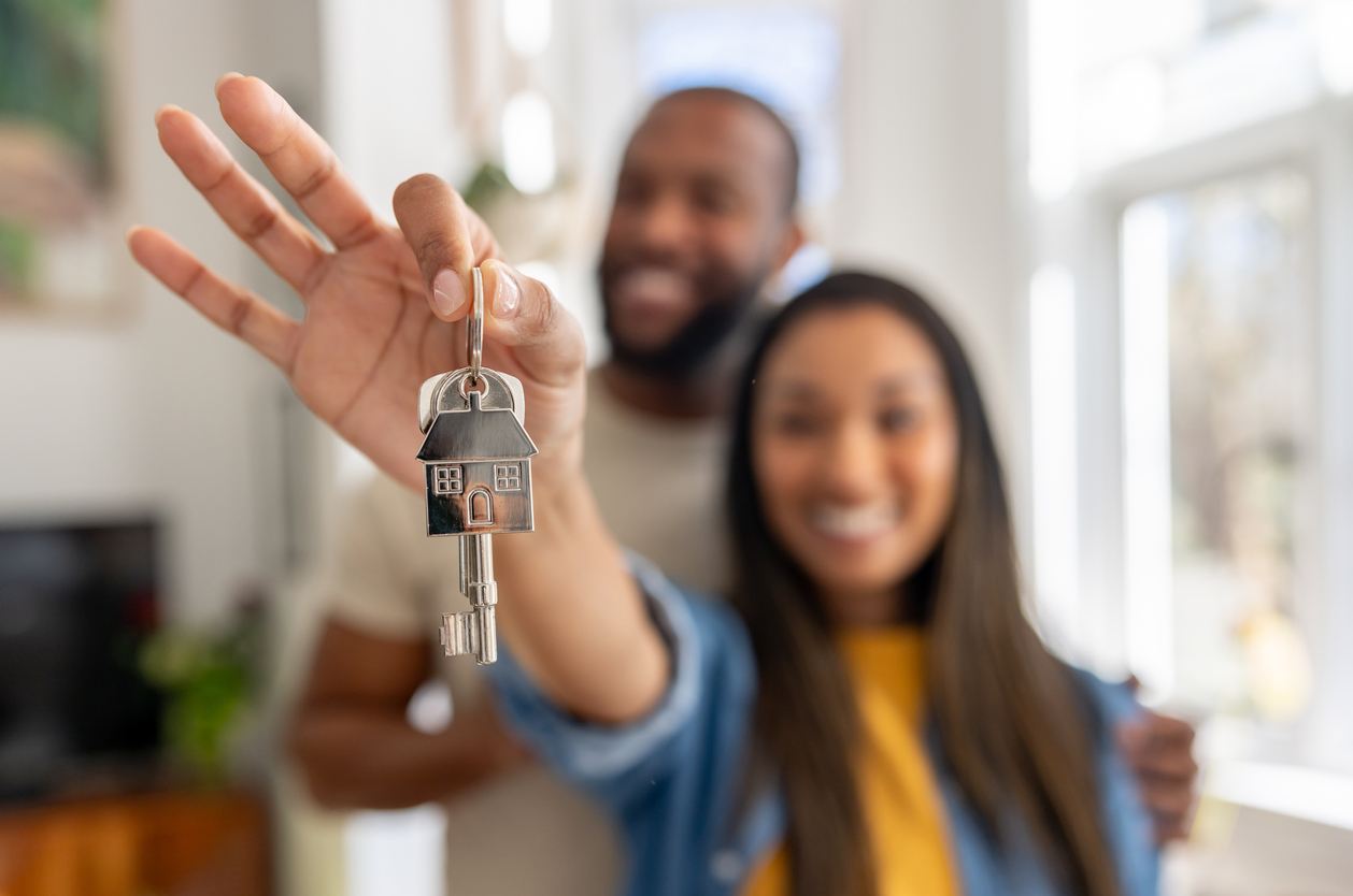 A couple holding up a set of house keys with a house key fob on it. 