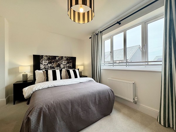 Second bedroom in a modern new‑build home at Westwood, Curbridge, featuring a double bed, patterned headboard, neutral tones, carpet flooring and a wide window.