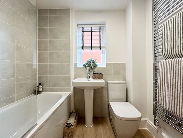 Stylish family bathroom in a modern new‑build home at Westwood, Curbridge, with a bath and overhead shower, pedestal sink, toilet, tiled walls and chrome towel radiator.