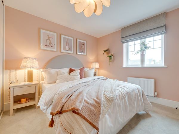 A photograph of a feminine double bedroom with pink walls and pink and white bedding on a double bed.