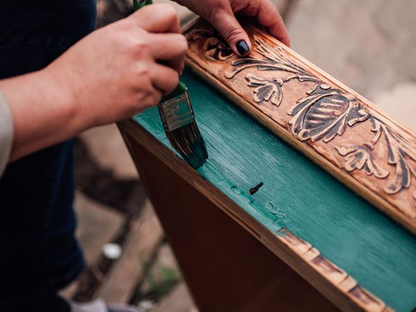 A person painting an old piece of furniture in a bright teal colour. 