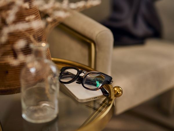 A close up of a pair of glasses and a phone on a brass and glass coffee table in a chic modern home.