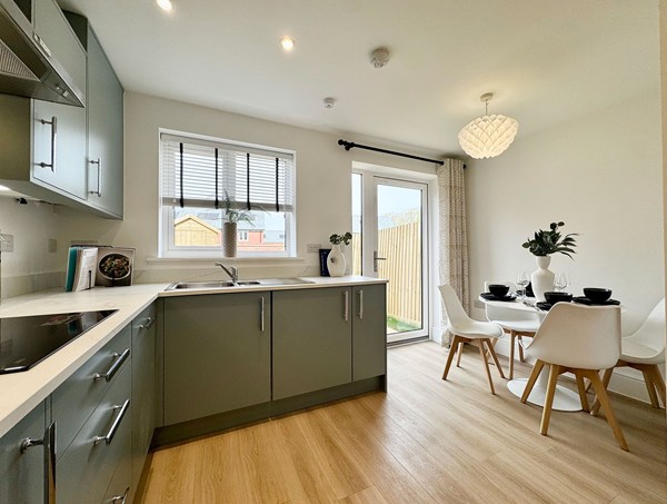 Open‑plan kitchen and dining area in a modern new‑build home at Westwood, Curbridge, featuring green fitted cabinets, integrated appliances, wood‑effect flooring and patio doors to the garden.