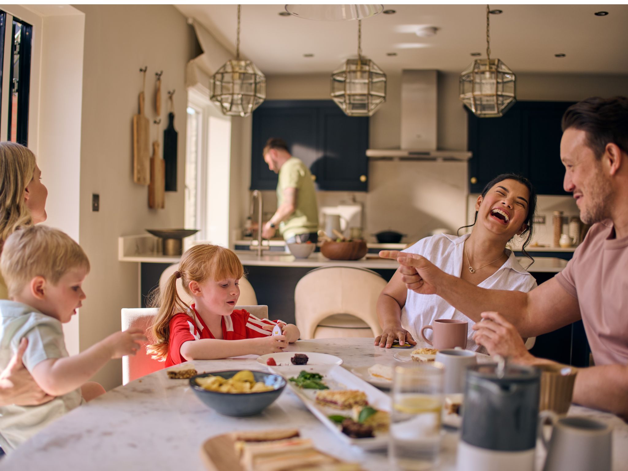 A family and friends having lunch at the dining table in a Charles Church home in an open-plan kitchen space.