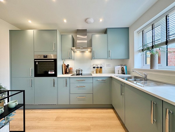 Modern fitted kitchen at Westwood, Curbridge, with green cabinetry, integrated oven and hob, stainless steel extractor, ample worktop space and recessed ceiling lighting.