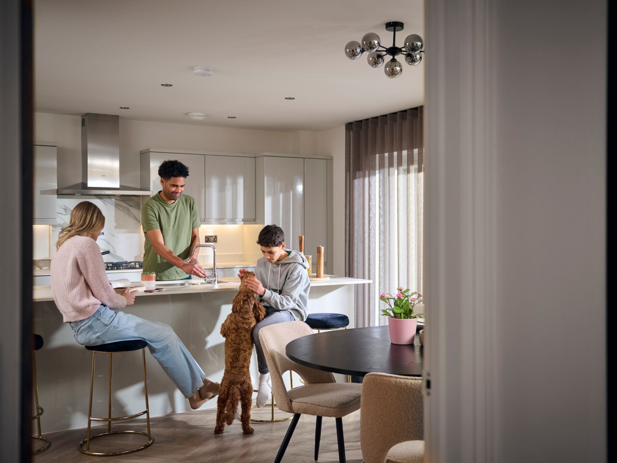 A man and a woman sitting at a breakfast island in a modern Charles Church home with their son, who is playing with a dog.