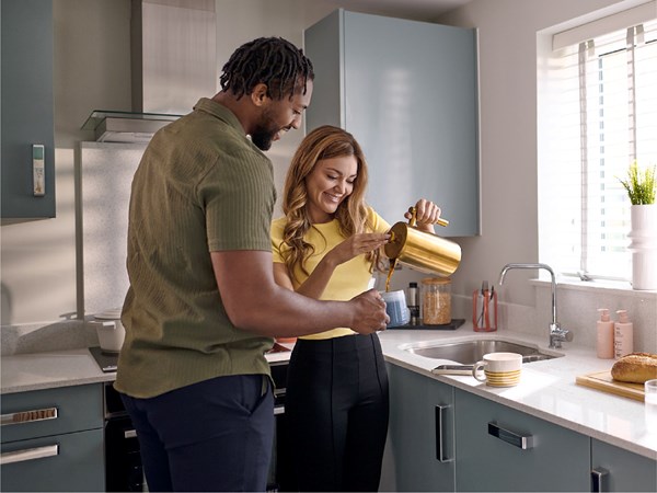 A smiling couple pouring coffee in a modern kitchen with sunlight streaming in the window. 
